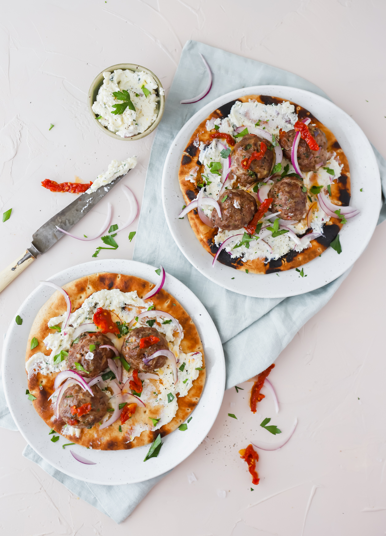 2 baked meatball pita wraps on a white surface garnished with sundried tomatoes and ricotta cheese spread