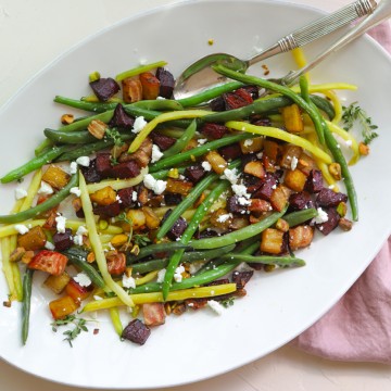 green beans and roasted beets sprinkled with goat cheese and pistachios on a white platter against a white backdrop