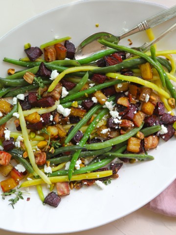 green beans and roasted beets sprinkled with goat cheese and pistachios on a white platter against a white backdrop