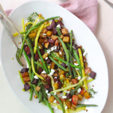 green beans and roasted beets sprinkled with goat cheese and pistachios on a white platter against a white backdrop