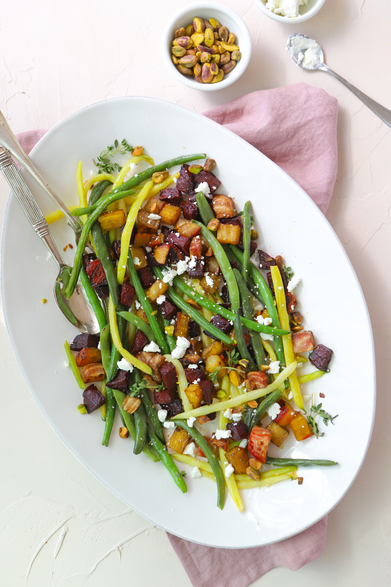 green beans and roasted beets sprinkled with goat cheese and pistachios on a white platter against a white backdrop 