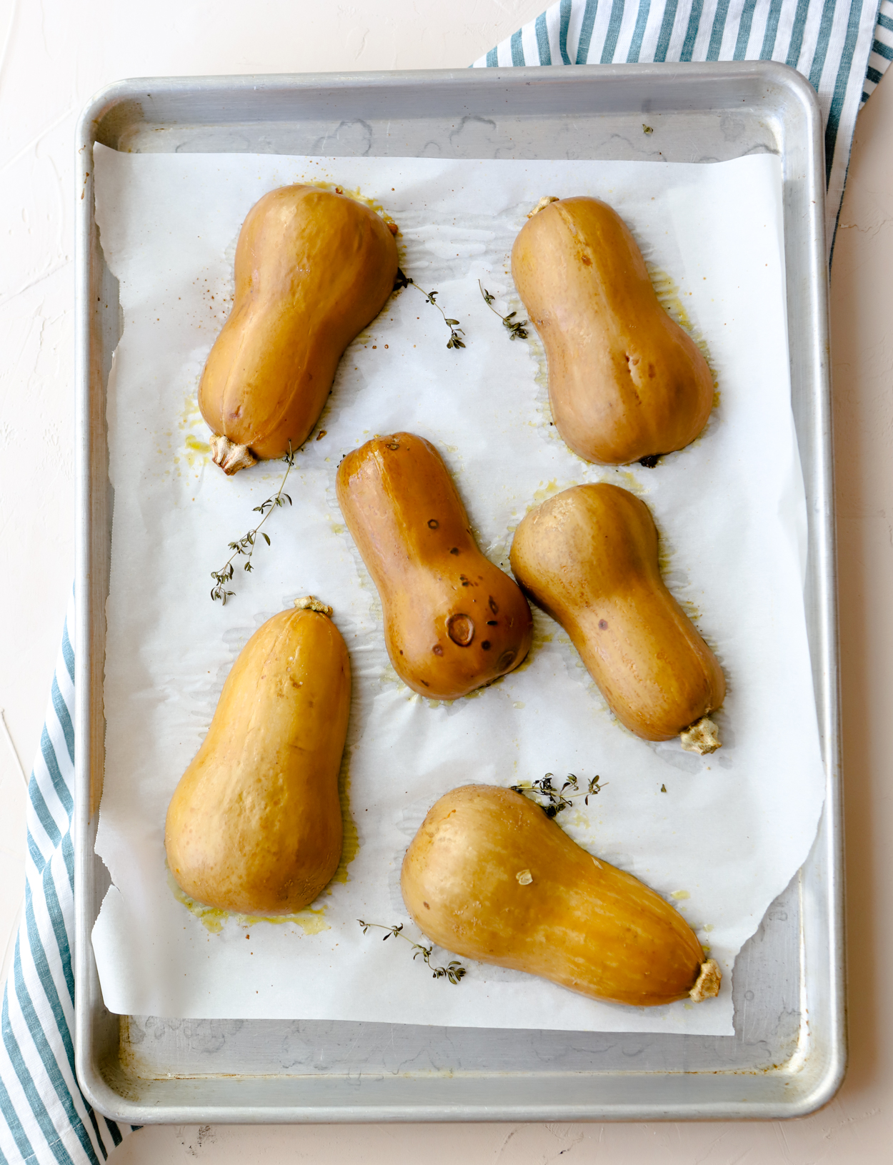 mini squash cut in half flesh side down on a baking sheet with thyme and olive oil