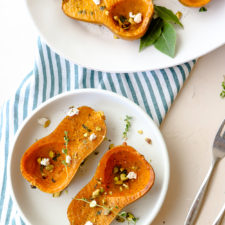 honeynut squash on a white plate sprinkled with goat cheese and pistachios