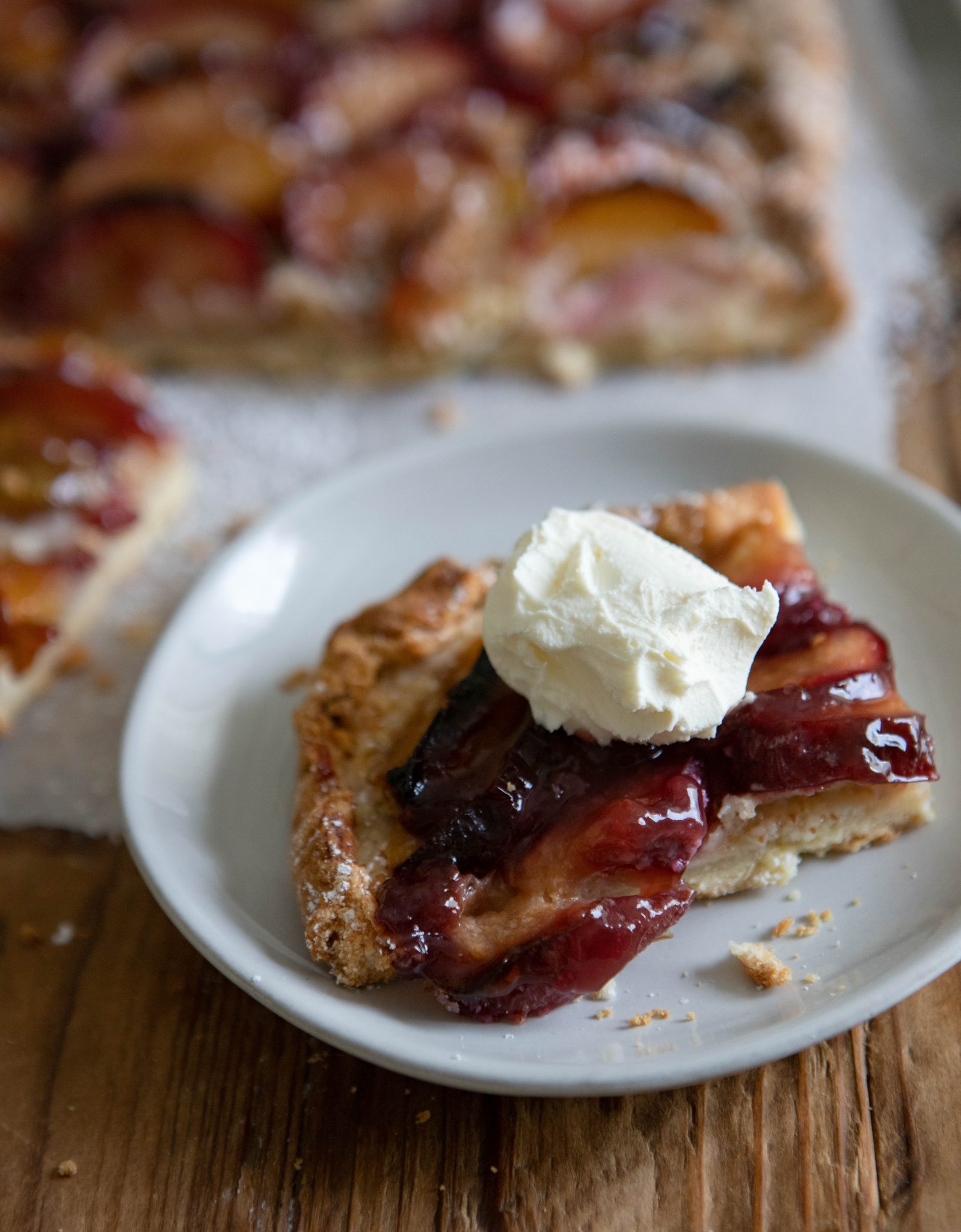 close up of a piece of plum tart on a white plate, topped with mascarpone
