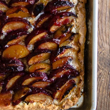close up of rustic plum tart out of the oven, sitting in a baking pan against a wood backdrop