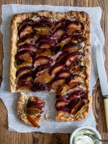 close up of a plum tart with a knife on top of parchment paper against a wooden backdrop