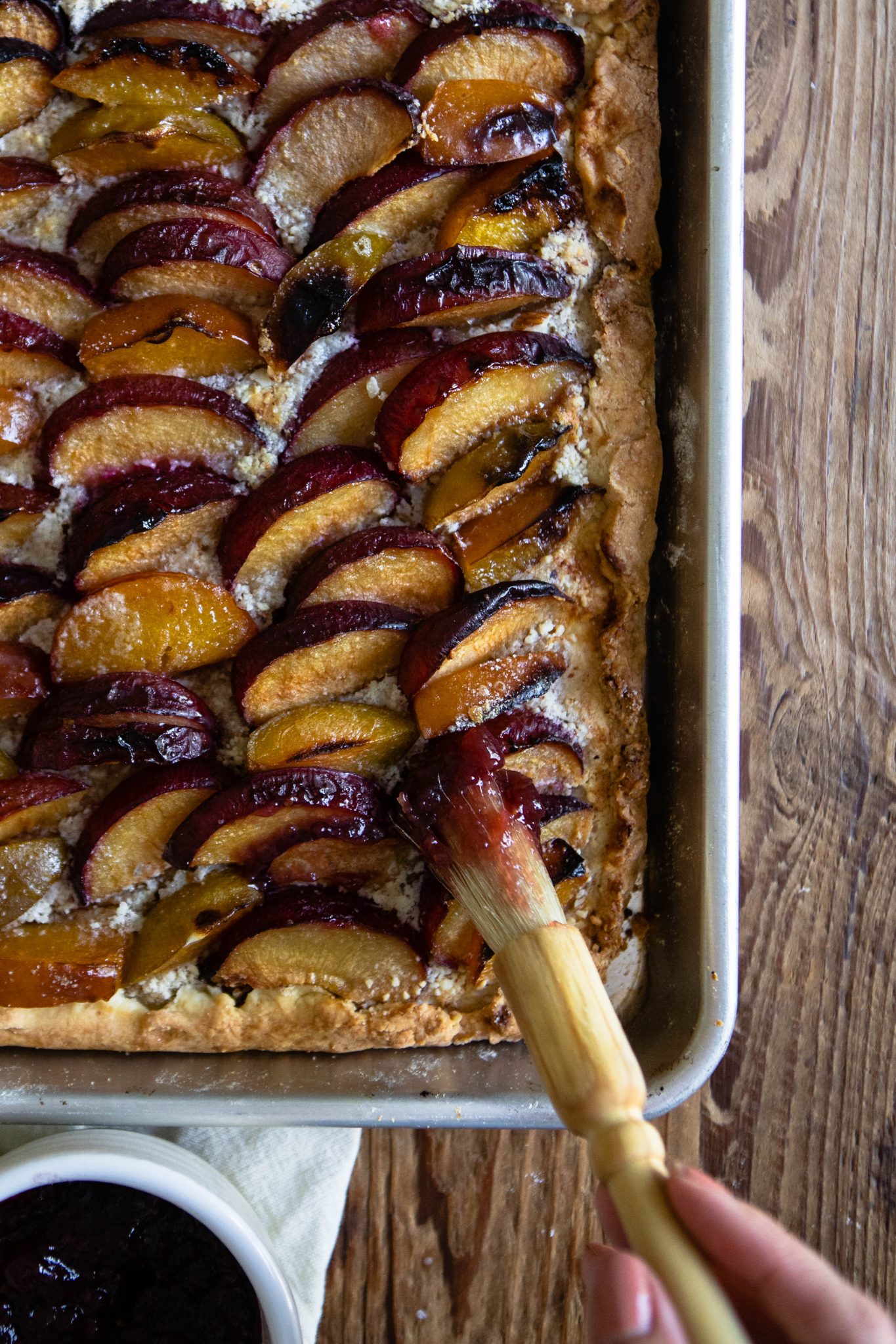 plum tart with raspberry jelly on a baking sheet against a wood backdrop