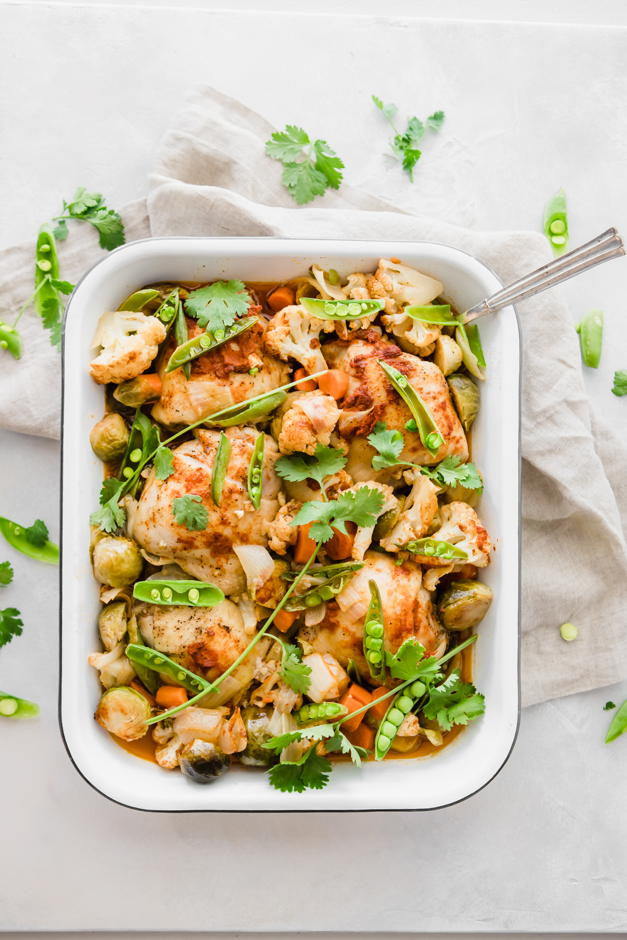 a white baking dish full of chicken and vegetables with coconut Thai curry sauce