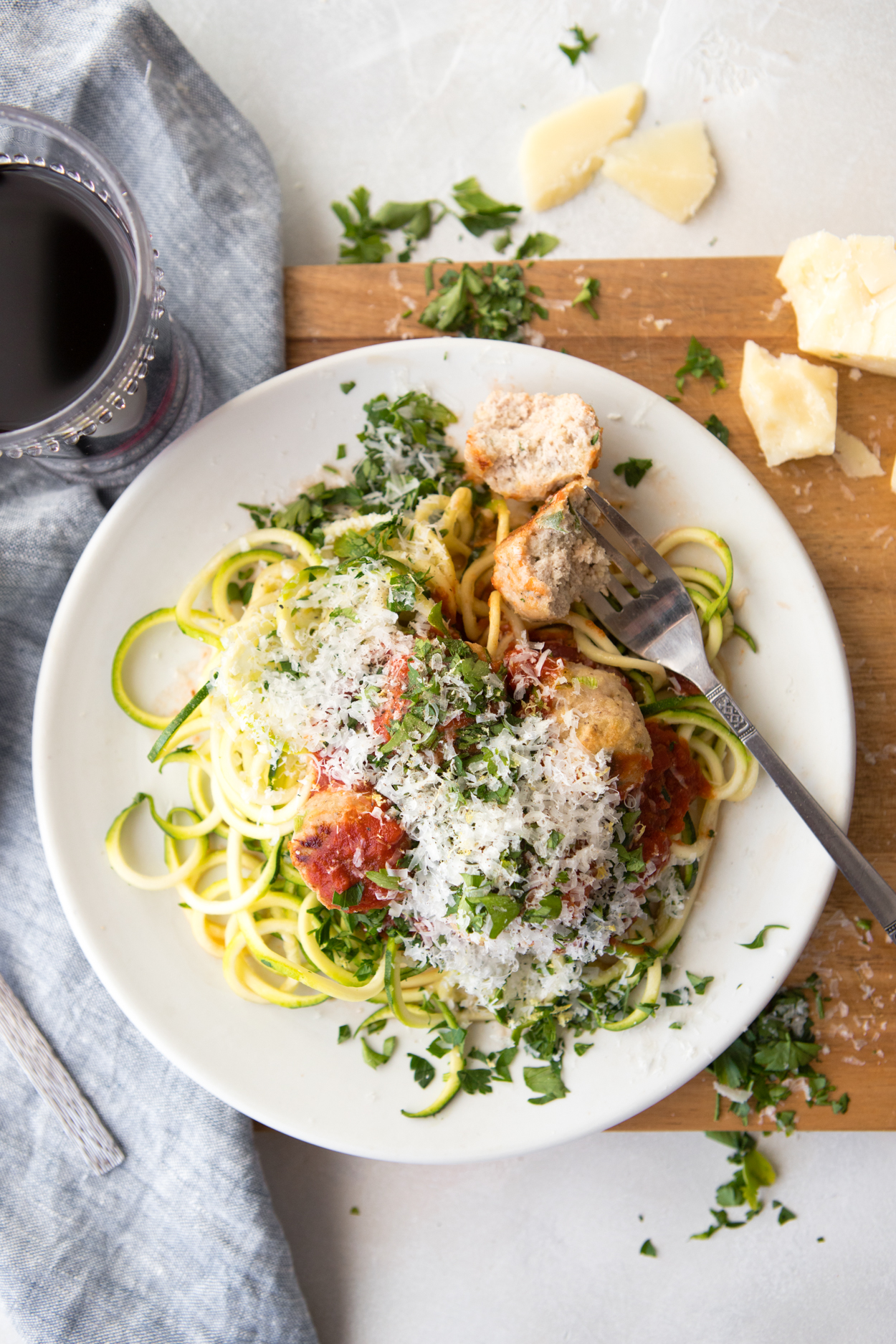 healthy turkey meatballs and zucchini noodles and marinara sauce on a white plate set on a wooden board with a glass of red wine 