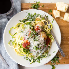 healthy turkey meatballs and zucchini noodles and marinara sauce on a white plate with a fork set on a wooden board with a glass of red wine