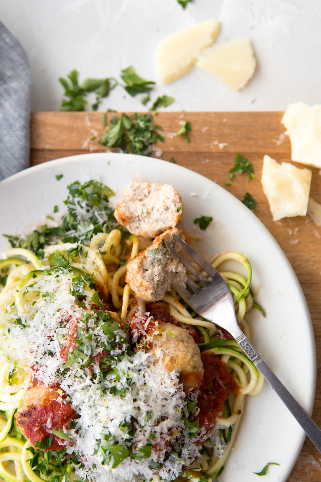 a fork digging into a plate of healthy turkey meatballs zucchini noodles and marinara sauce dished up on a white plate