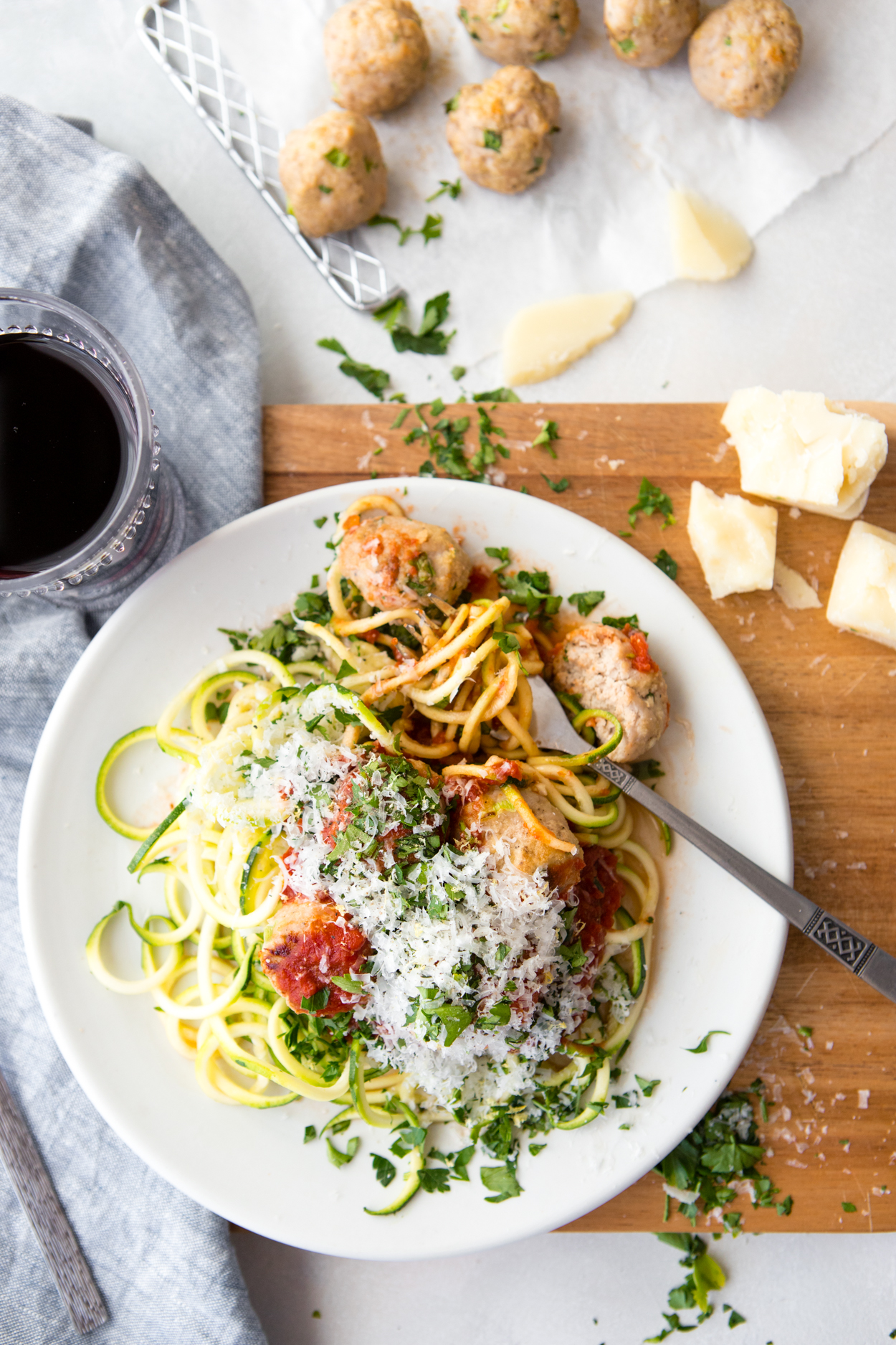 a tray of baked meatballs set next to a white round plate filled with zoodles, marinara sauce and healthy turkey meatballs