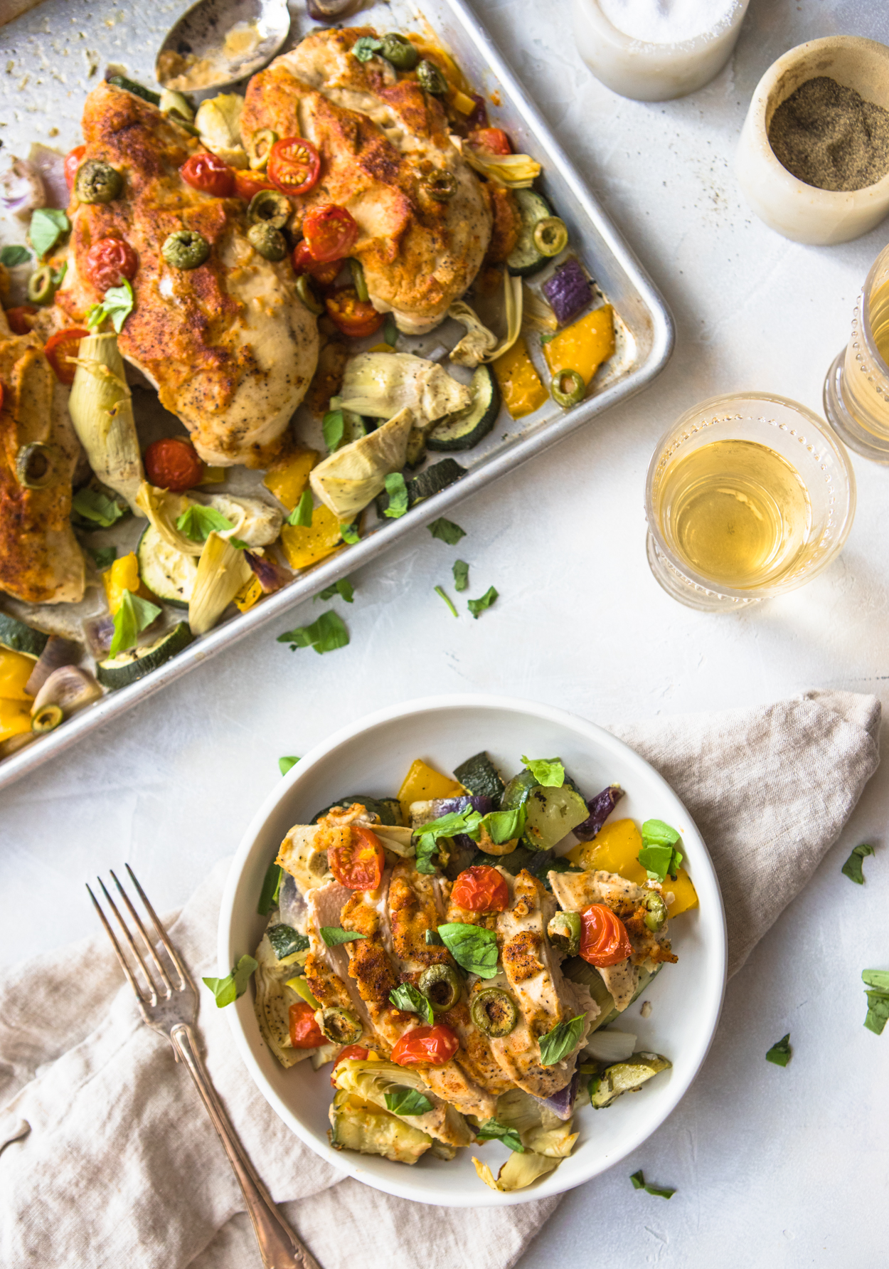 sliced chicken with hummus and roasted vegetables on a white plate with fork and napkin 