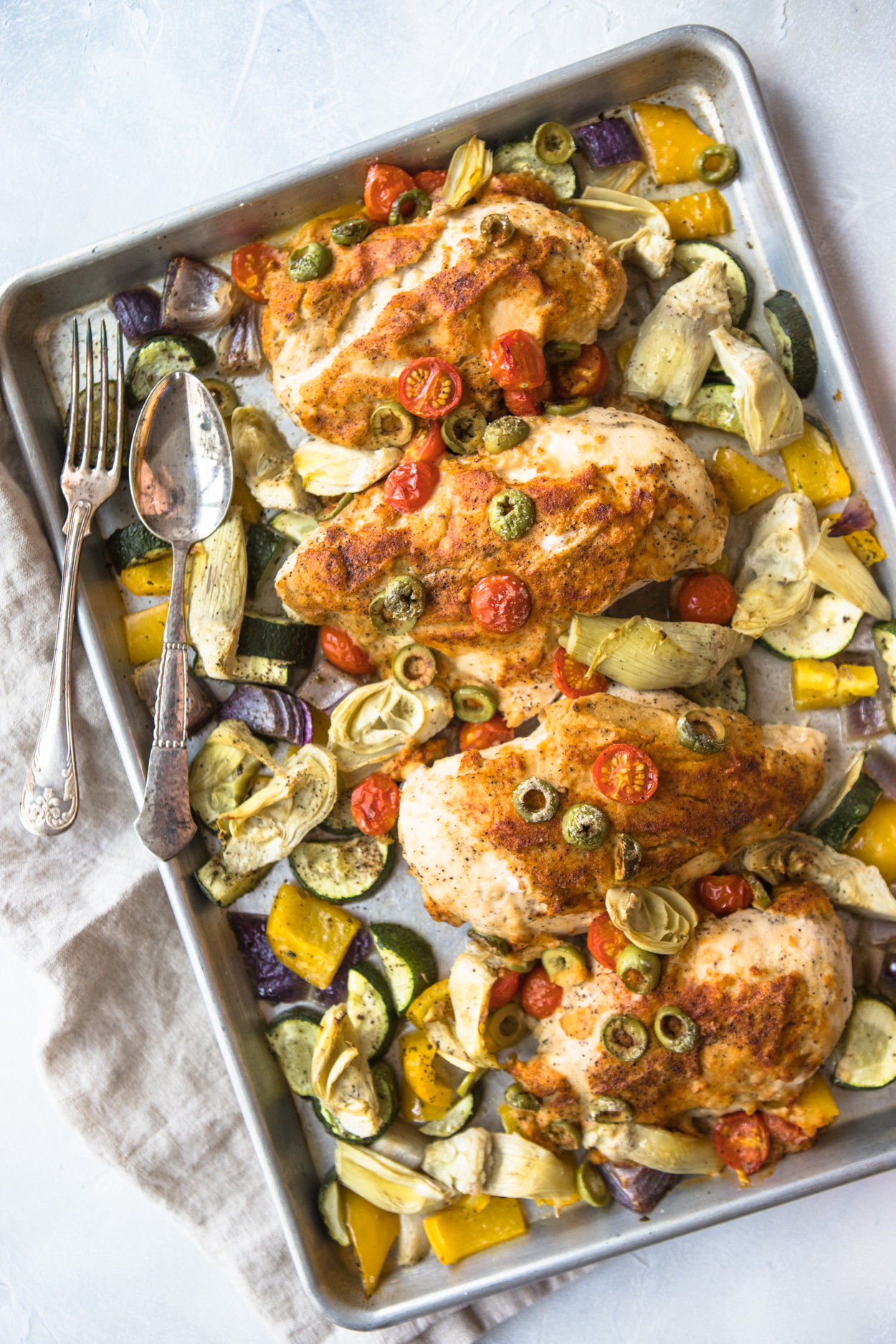 hummus crusted chicken breasts with vegetables on a metal sheet pan