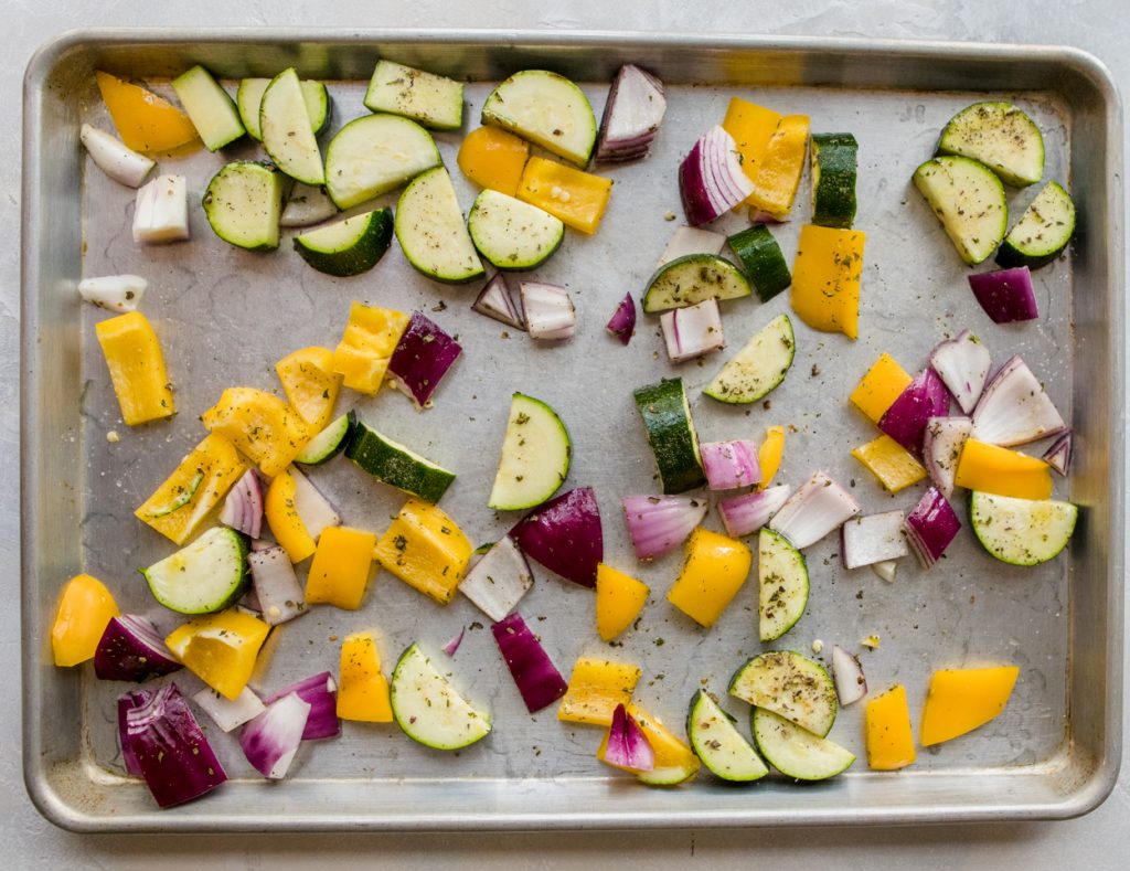cut up vegetables sprinkled with herbs on a rimmed baking sheet
