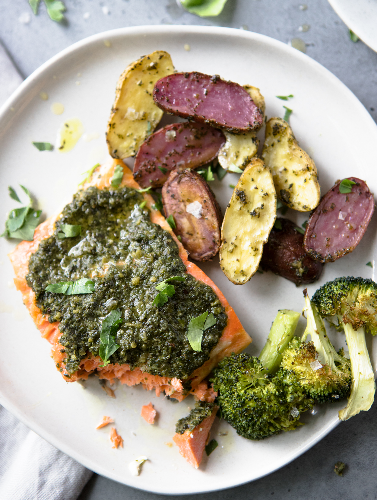 baked pesto salmon, potatoes and broccoli on a white round plate 