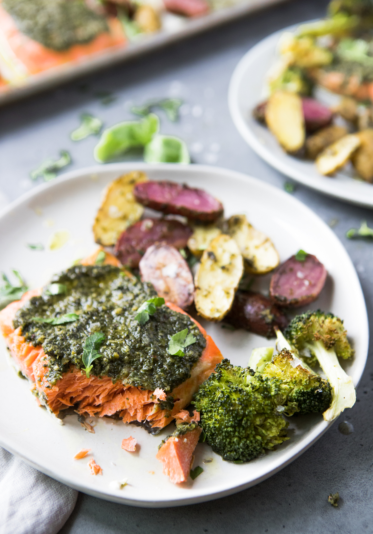 Baked salmon with pesto and broccoli and potatoes on a white round plate