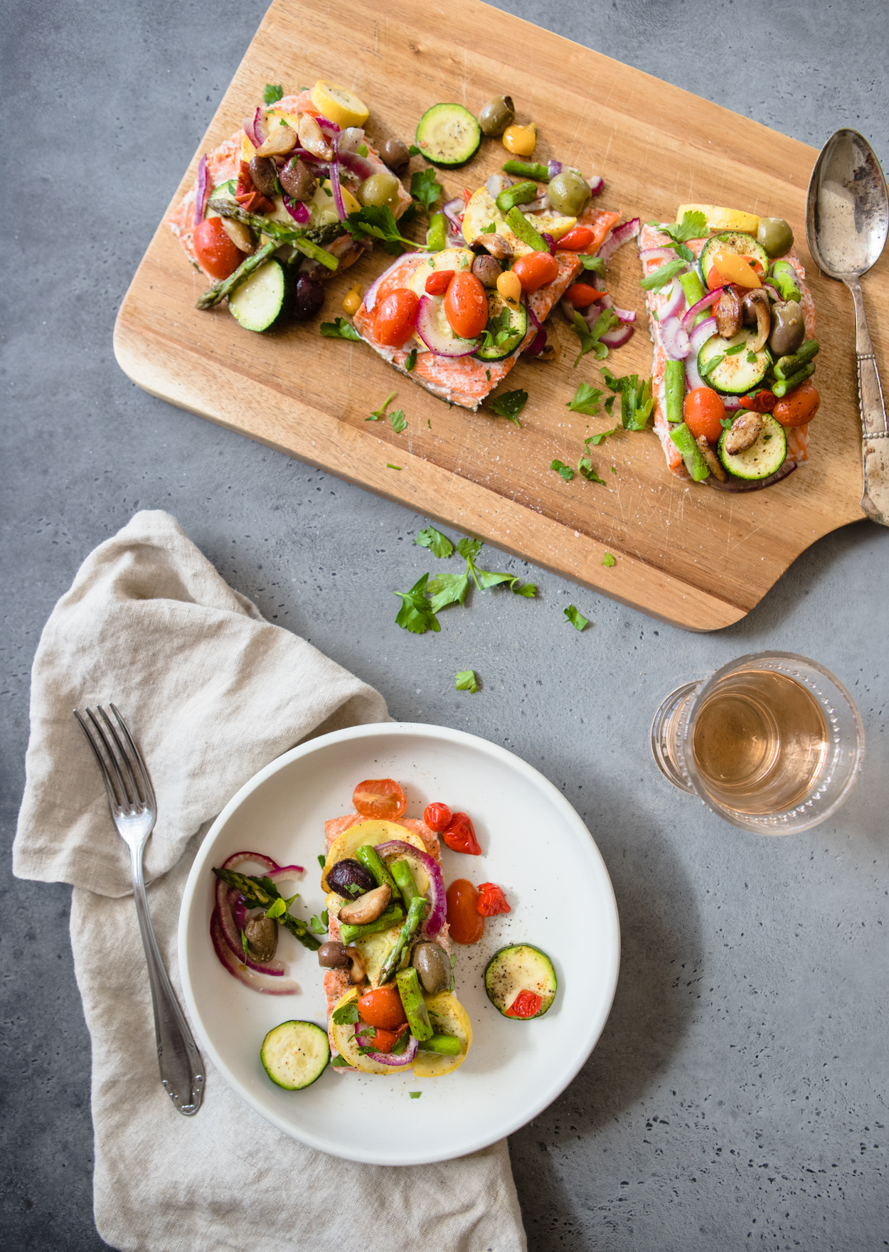 baked salmon and veggies on a white plate, a cutting board with three salmon fillets and veggies