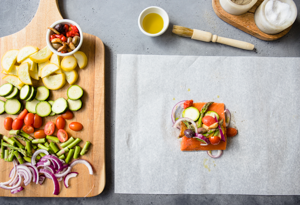 A piece of salmon topped with veggies on a sheet of parchment paper