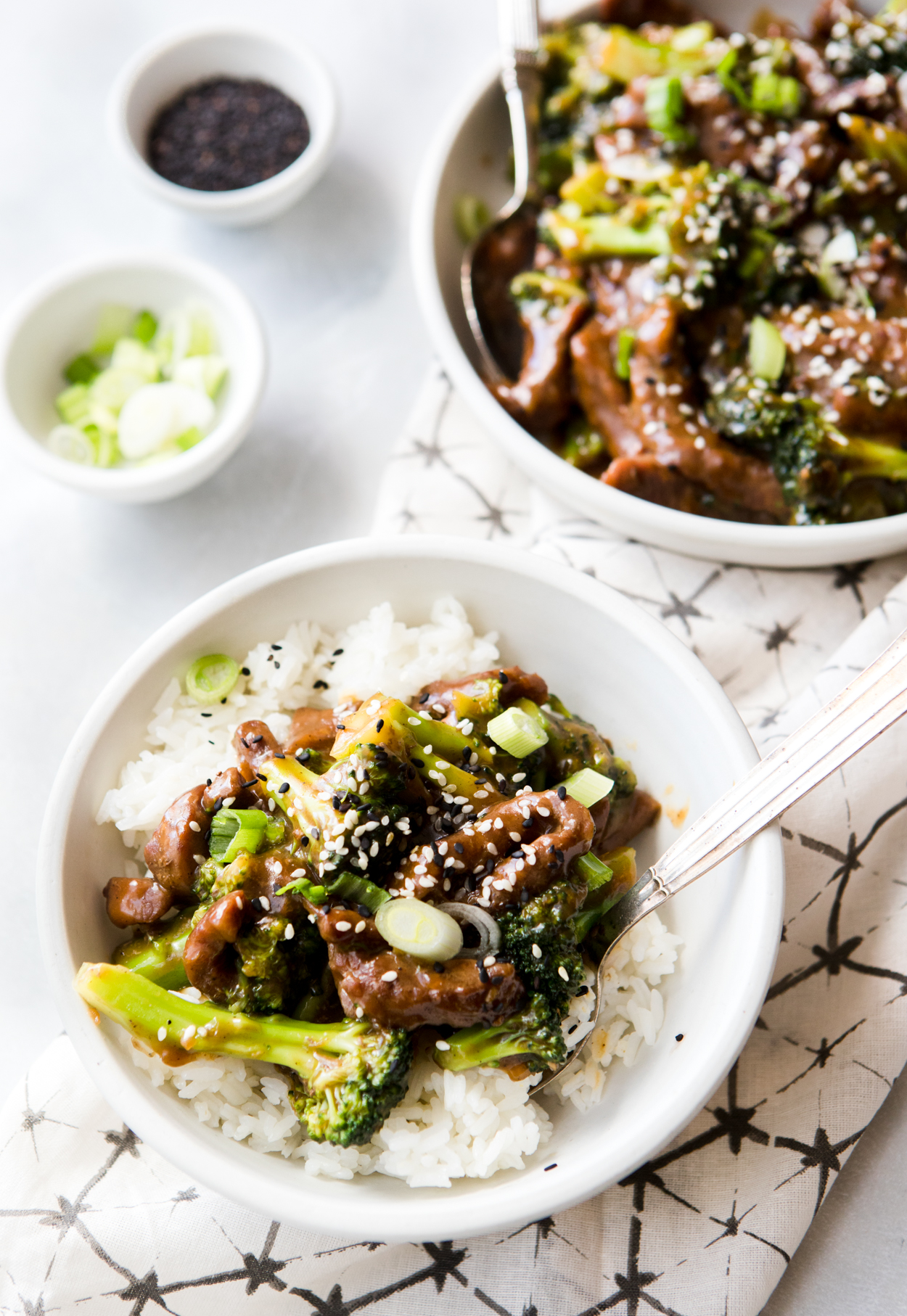 two bowls of Instant Pot Beef and Broccoli on a napkin garnished with sesame seed and green onions