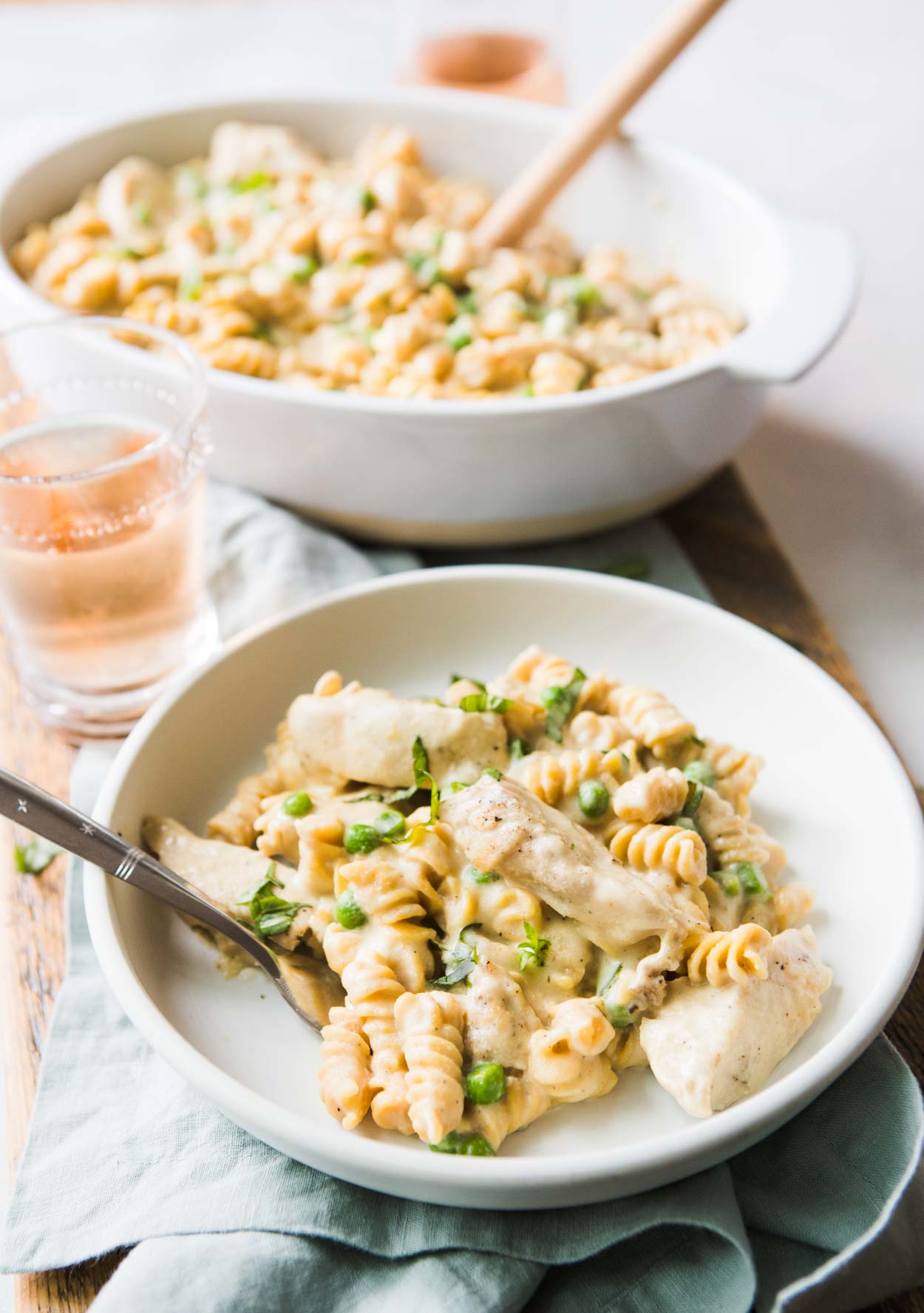 dairy free chicken alfredo in a white bowl with peas and basil