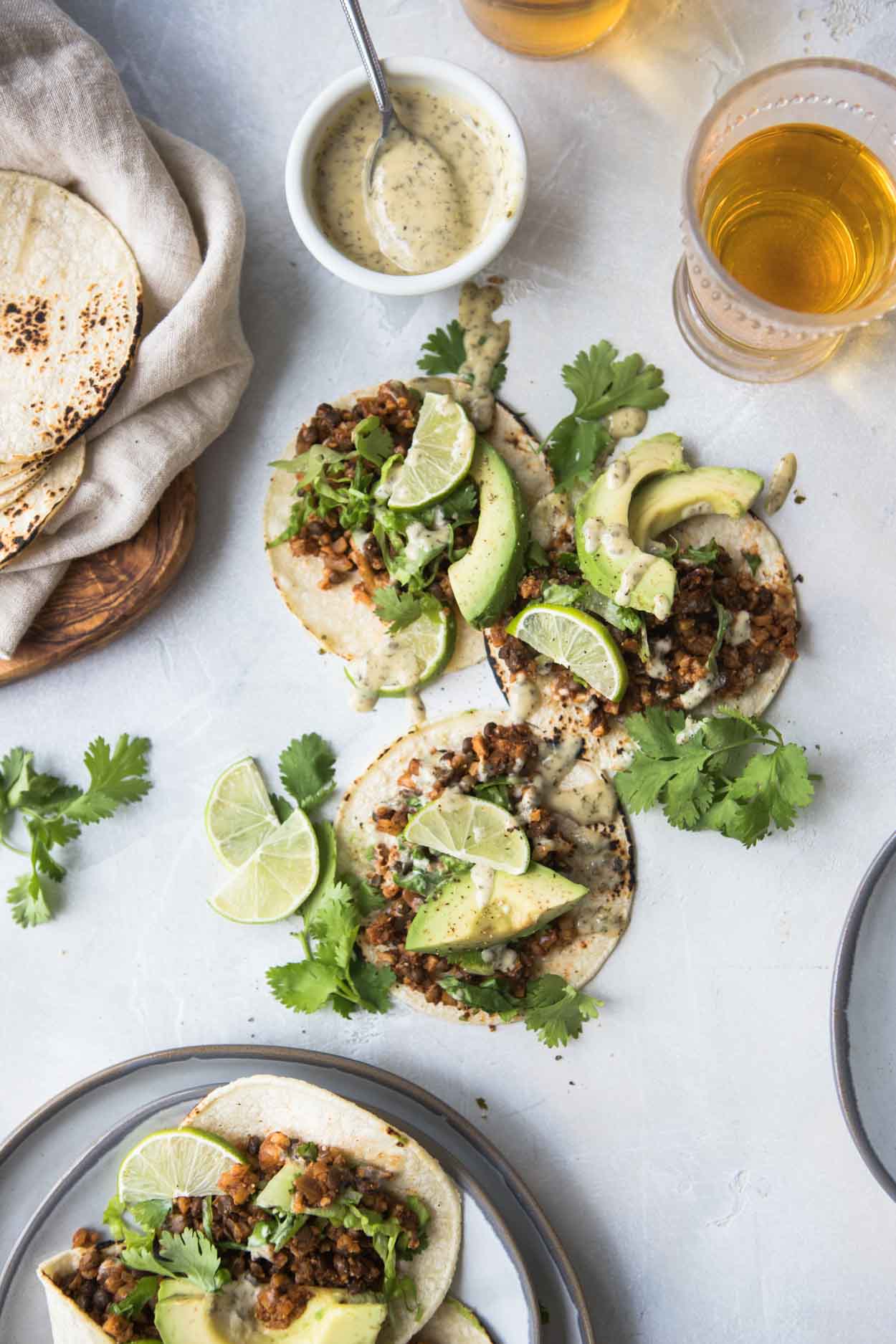 Glass of beer and vegan cauliflower and lentil tacos on a white background with round plates and charred tortillas