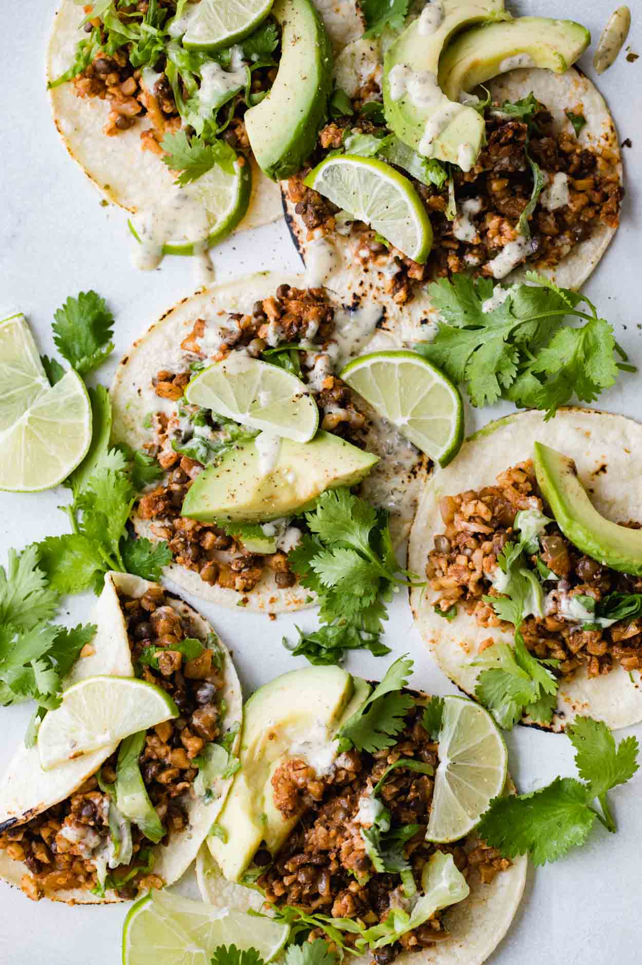 Cauliflower rice and lentil tacos on corn tortillas with limes, avocado and cilantro on a white board 