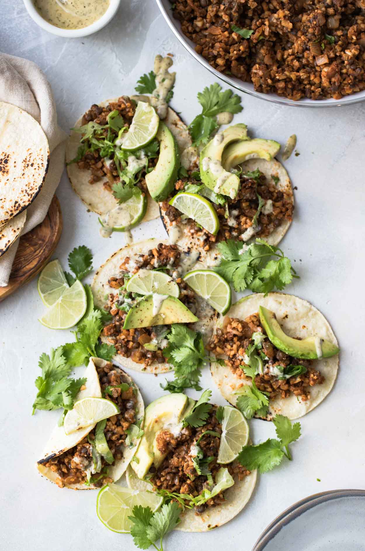 Cauliflower rice and lentil tacos on corn tortillas with limes, cilantro and avocado on a white board