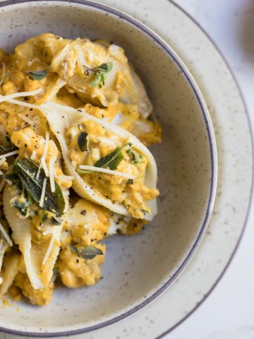Stuffed pasta shells in a cream colored bowl on a white background