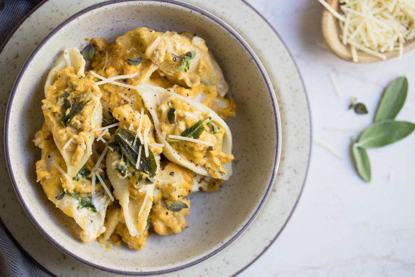 Stuffed pasta shells in a cream colored bowl on a white background
