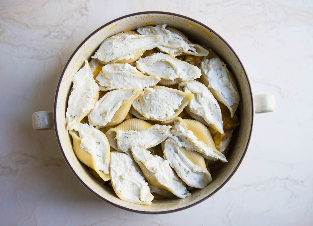 Stuffed pasta shells in a cream colored bowl on a white background