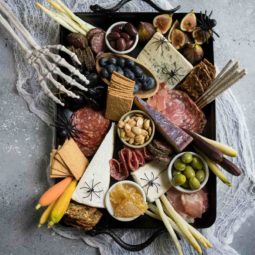 Charcuterie board on a black platter with spiders and skeleton hand on a gray board