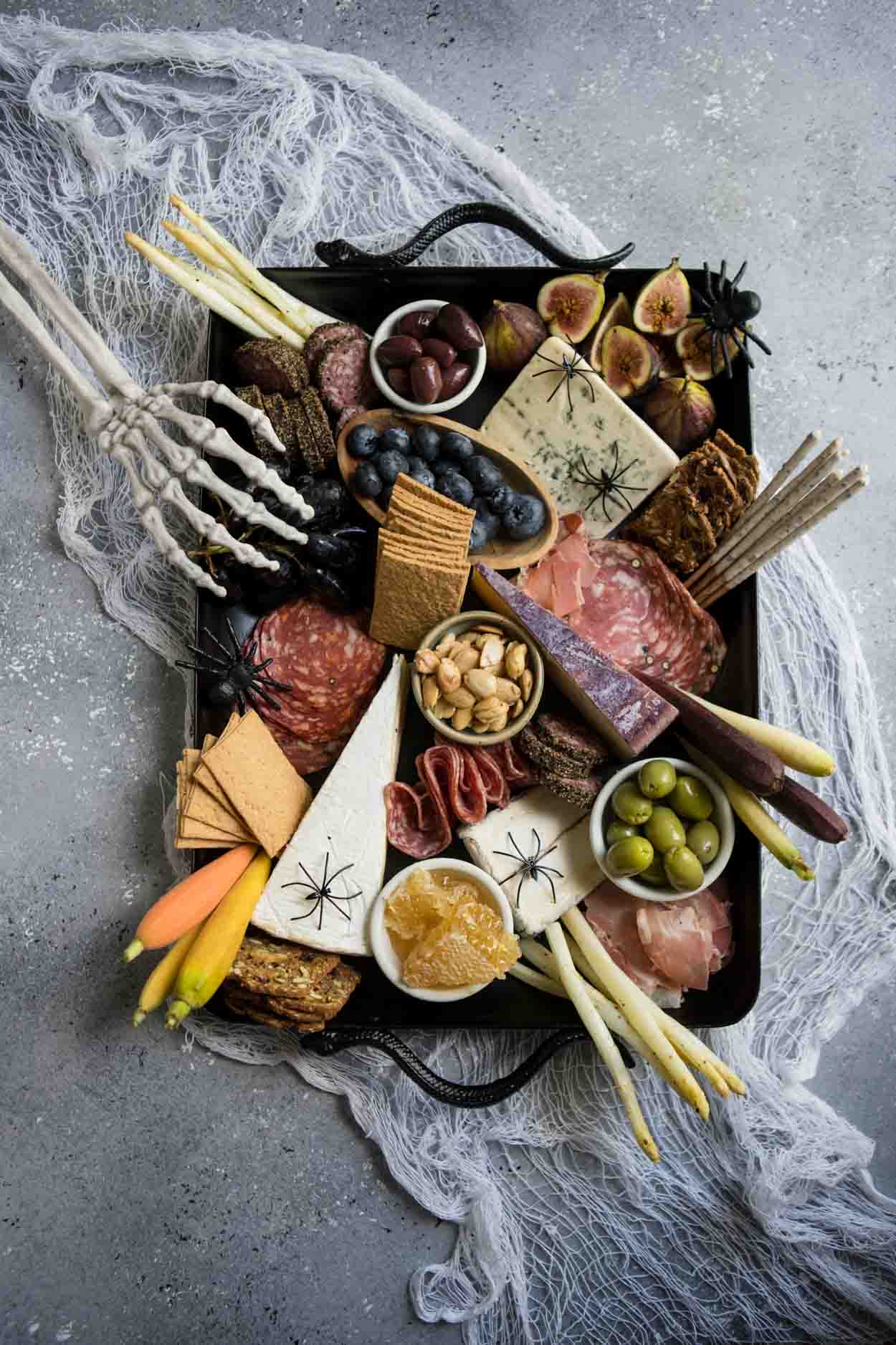 Halloween Charcuterie board on a black platter with spiders and skeleton hand on a gray board
