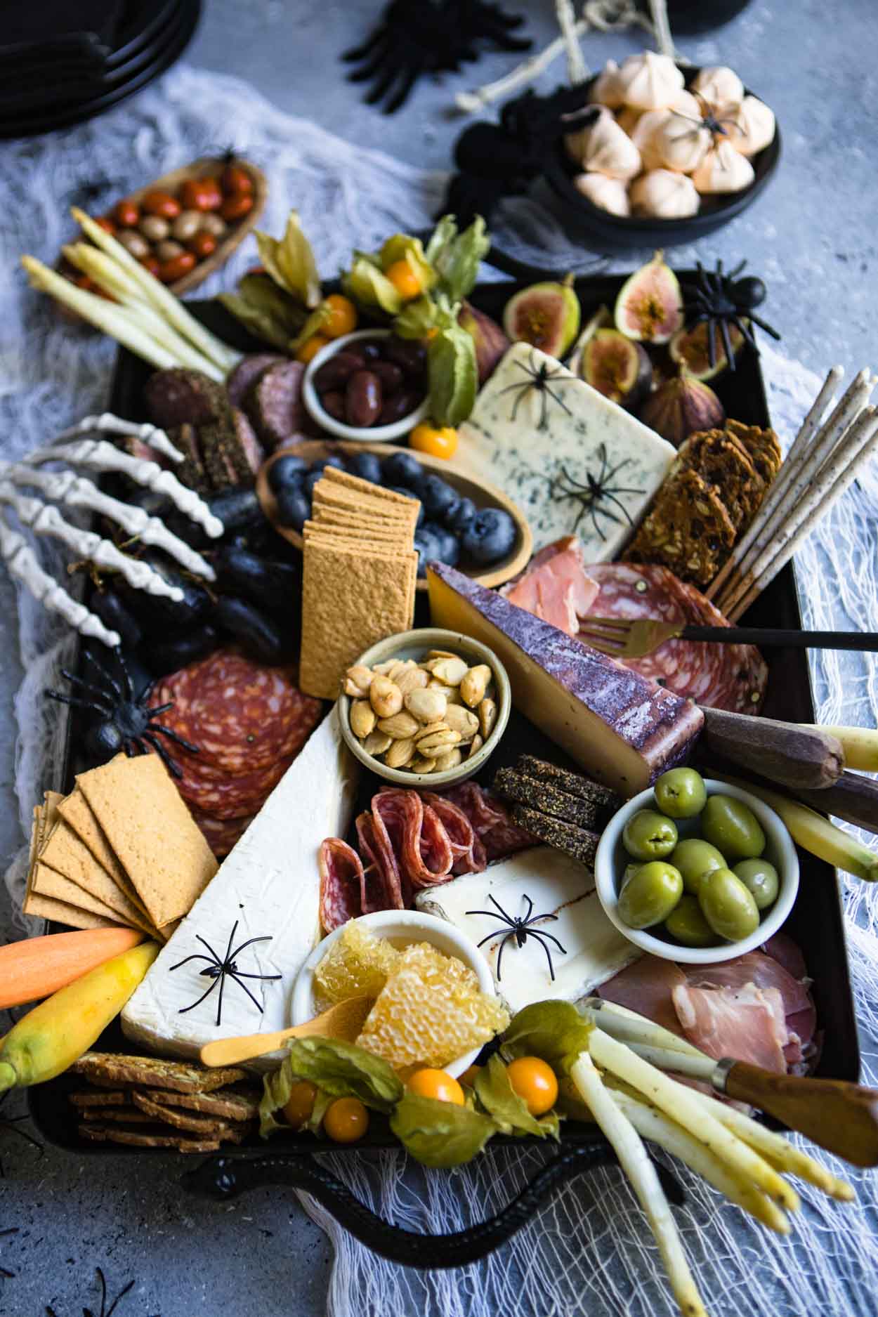 Charcuterie board on a black platter with spiders and skeleton hand on a gray board