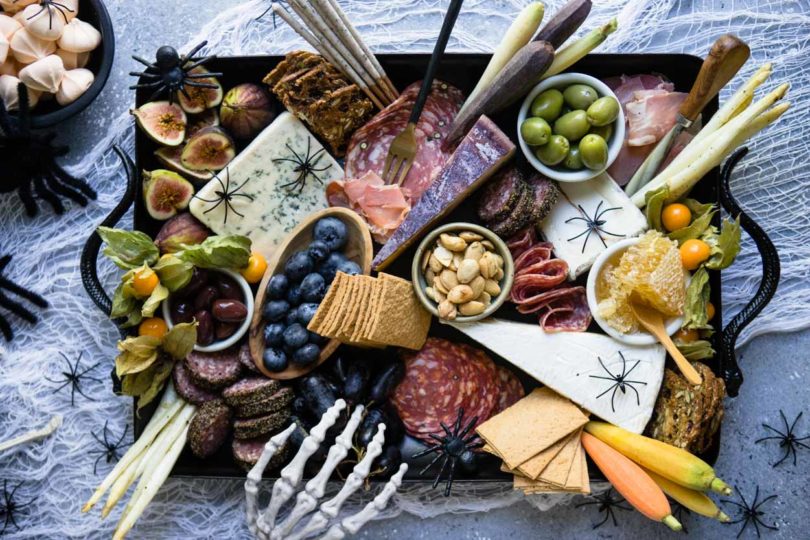 Charcuterie board on a black platter with spiders and skeleton hand on a gray board