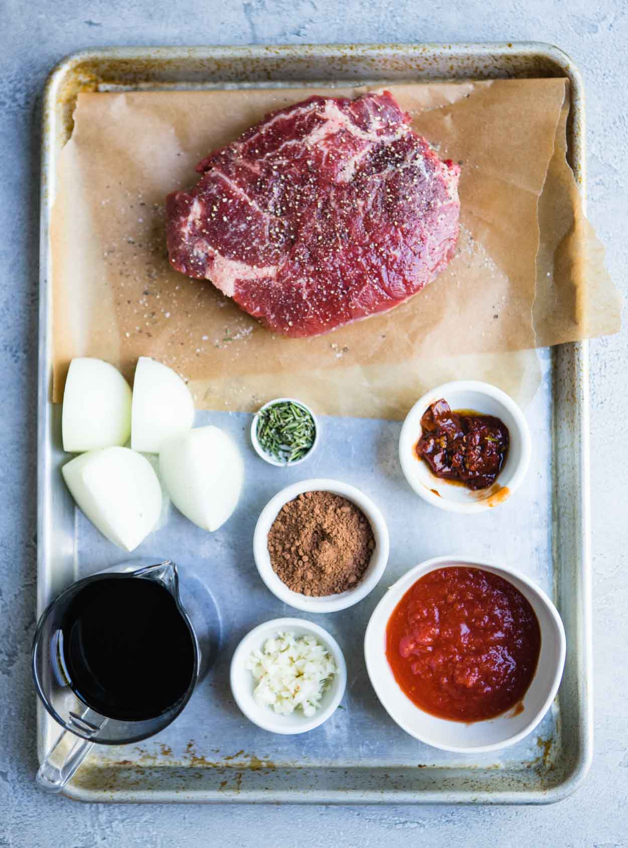 Pot roast uncooked and other cooking ingredients on a baking sheet