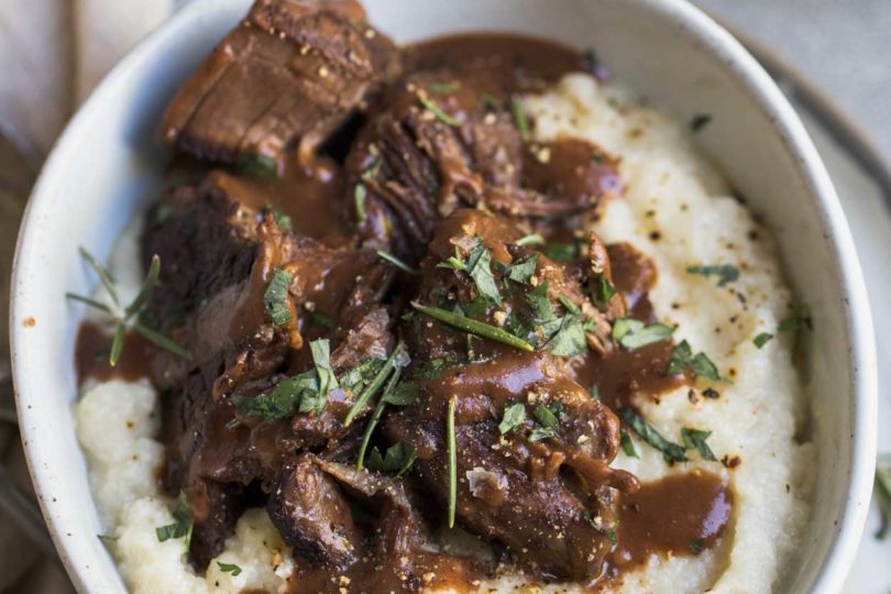 Pot roast and mashed cauliflower with gravy and herbs in a white bowl