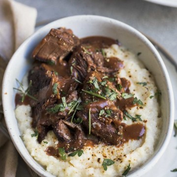 Pot roast and mashed cauliflower with gravy and herbs in a white bowl
