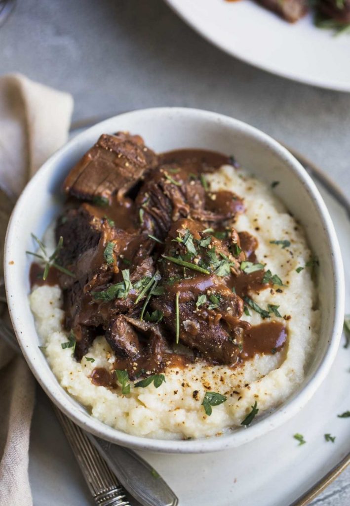 Pot roast and mashed cauliflower with gravy and herbs in a white bowl