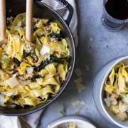 Wide egg noodles with sausage, kale and fennel in a black cast iron pot and on 2 gray bowls on a gray surface