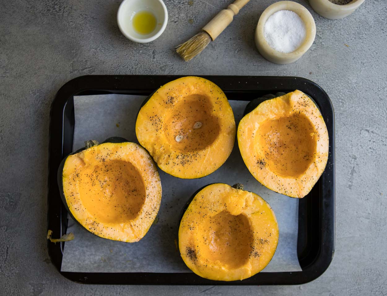 Raw acorn squash brushed with olive oil and salt and pepper on a gray background