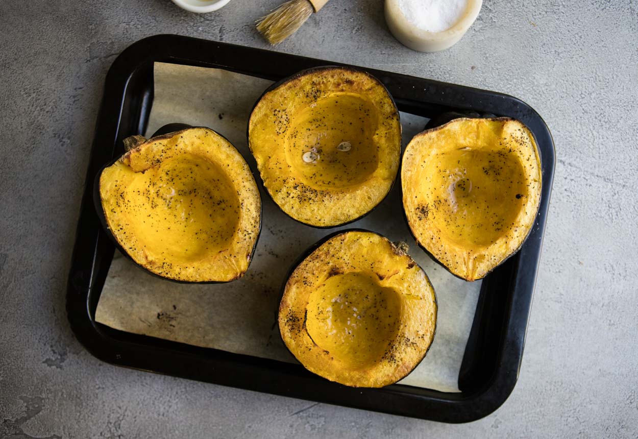 Roasted acorn squash on a black baking sheet on a gray surface