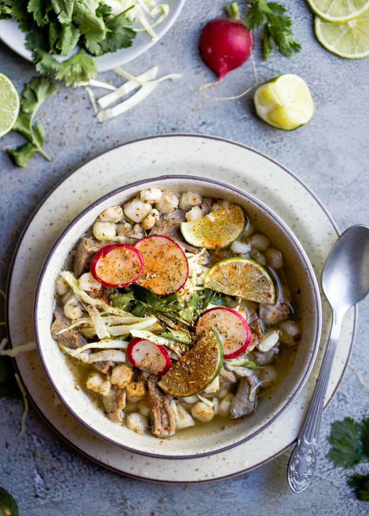 New Mexico posole soup in a beige bowl garnished with radishes, limes, and cabbage