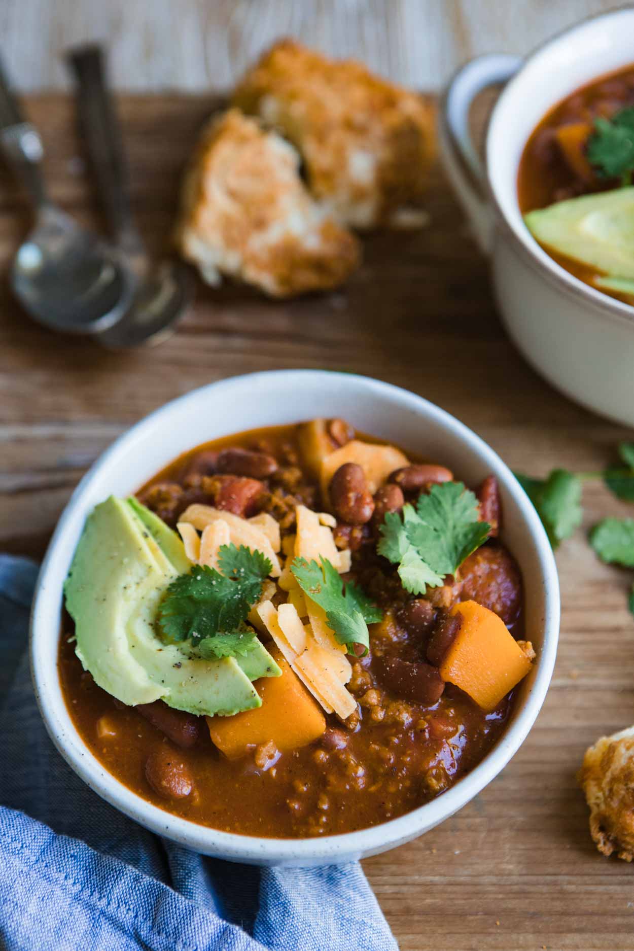 a bowl of vegetarian sweet potato chili with avocado, cheese and cilantro garnish