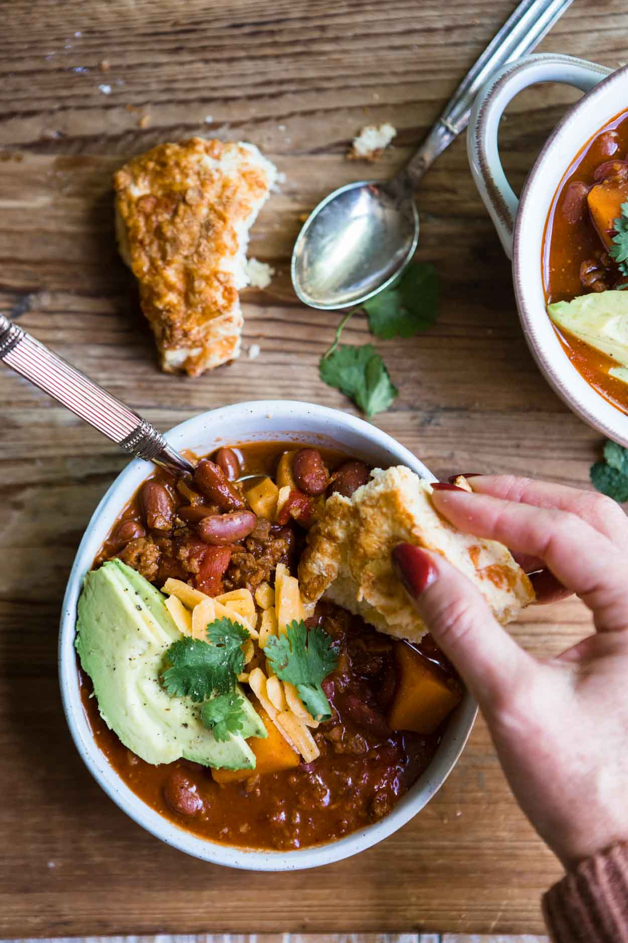 a woman's hand dunking a piece of biscuit into a bowl of sweet potato vegetarian chili