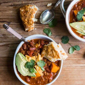 a bowl of sweet potato vegetarian chili with a spoon and cheddar biscuit