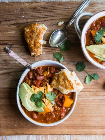 a bowl of sweet potato vegetarian chili with a spoon and cheddar biscuit