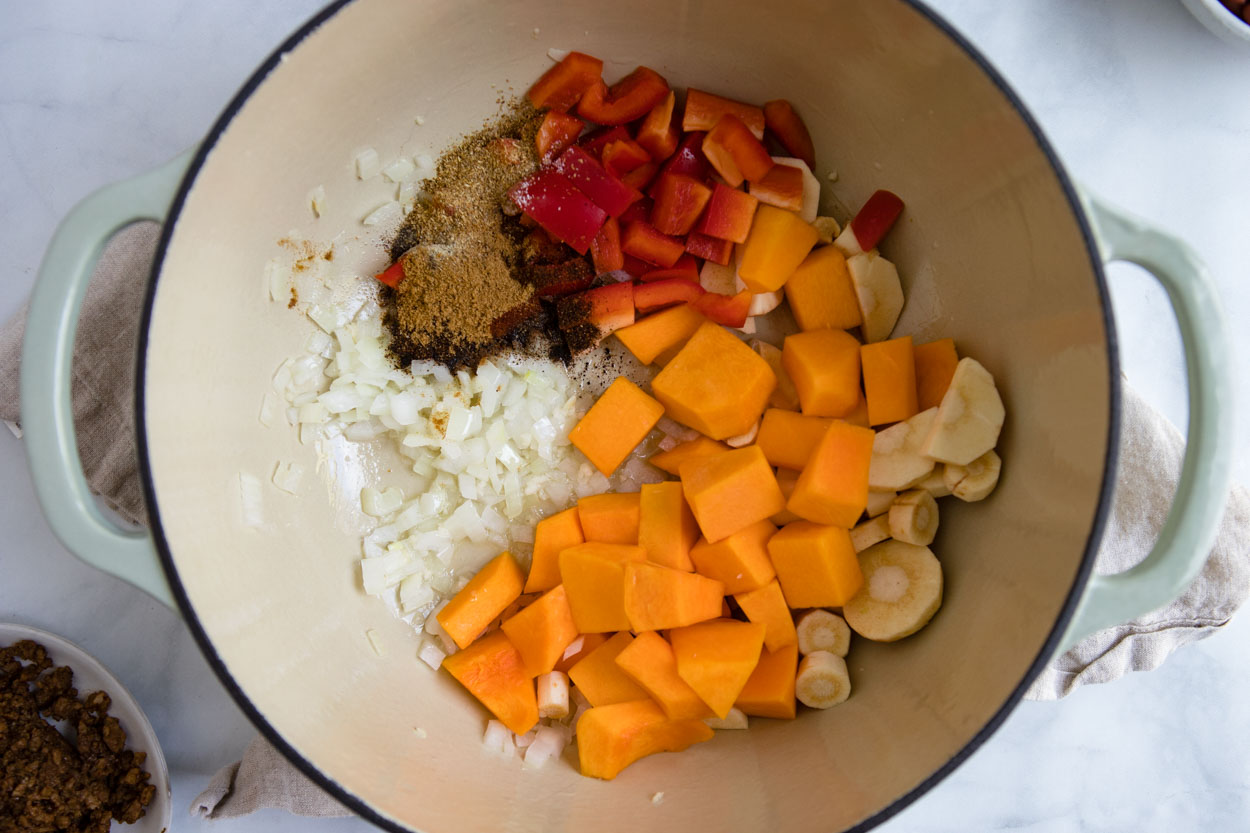 close up of spices and veggie chili ingredients in a round dutch oven pot