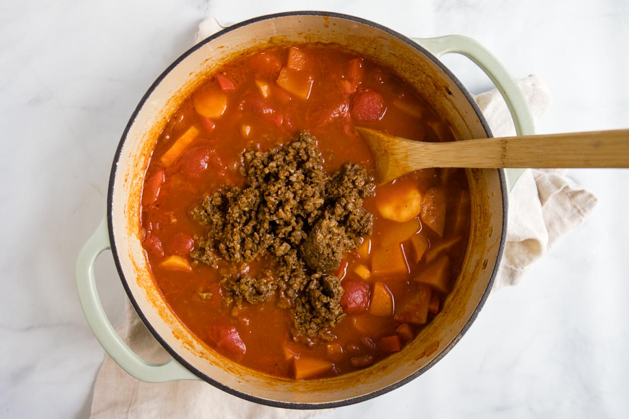 sweet potato vegetarian chili ingredients in a dutch oven pot with veggie crumbles being stirred in