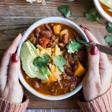 vegetarian sweet potato chili in a bowl garnished with avocado and cheese